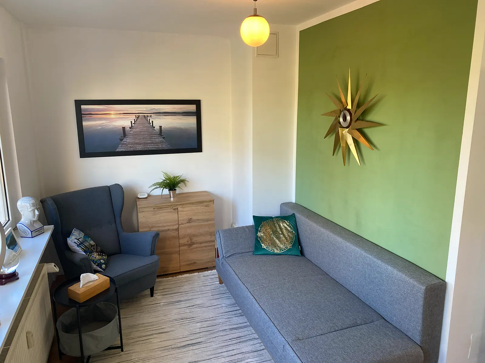 Praxisraum in Düsseldorf mit grauem Sessel und Liege vor grüner Wand